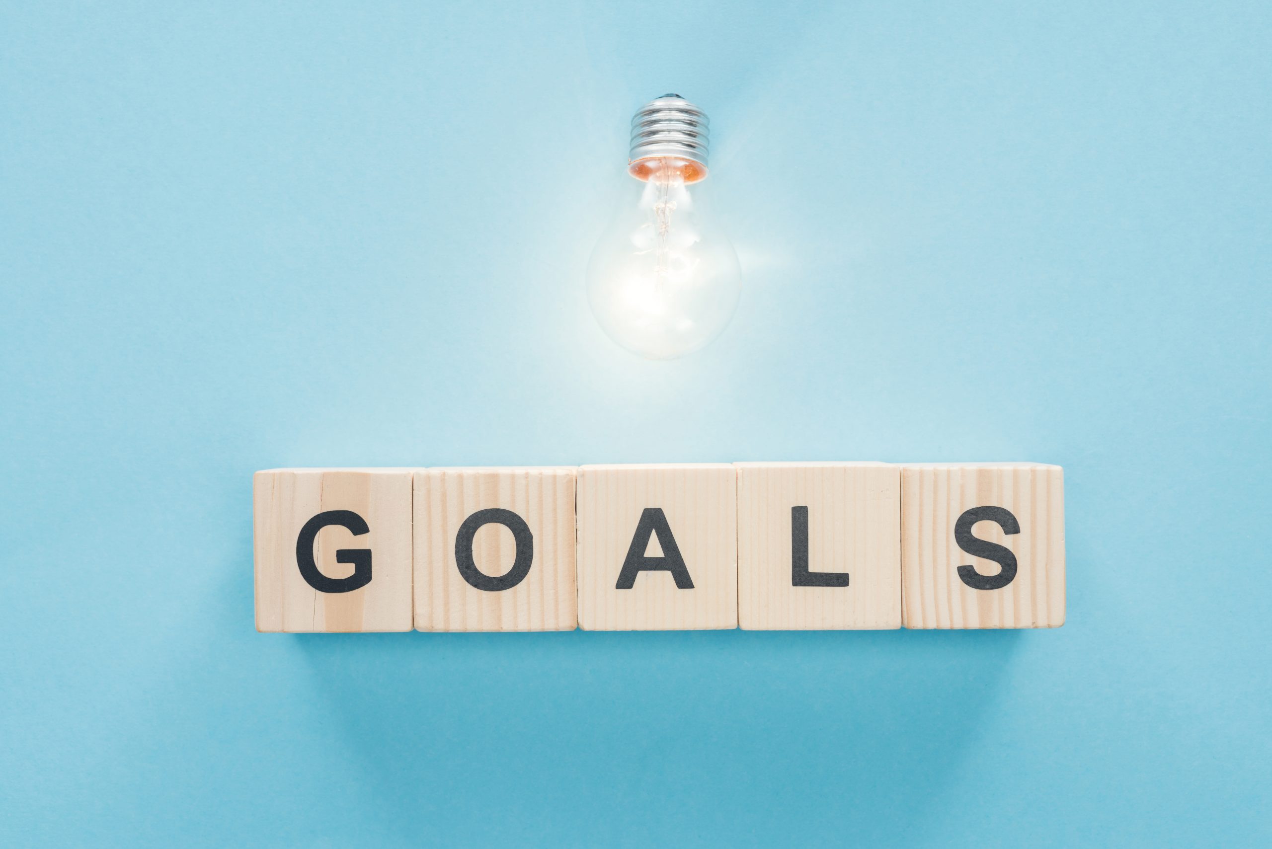 Glowing lightbulb above the word "goals" spelled out in wooden blocks against a light blue background.