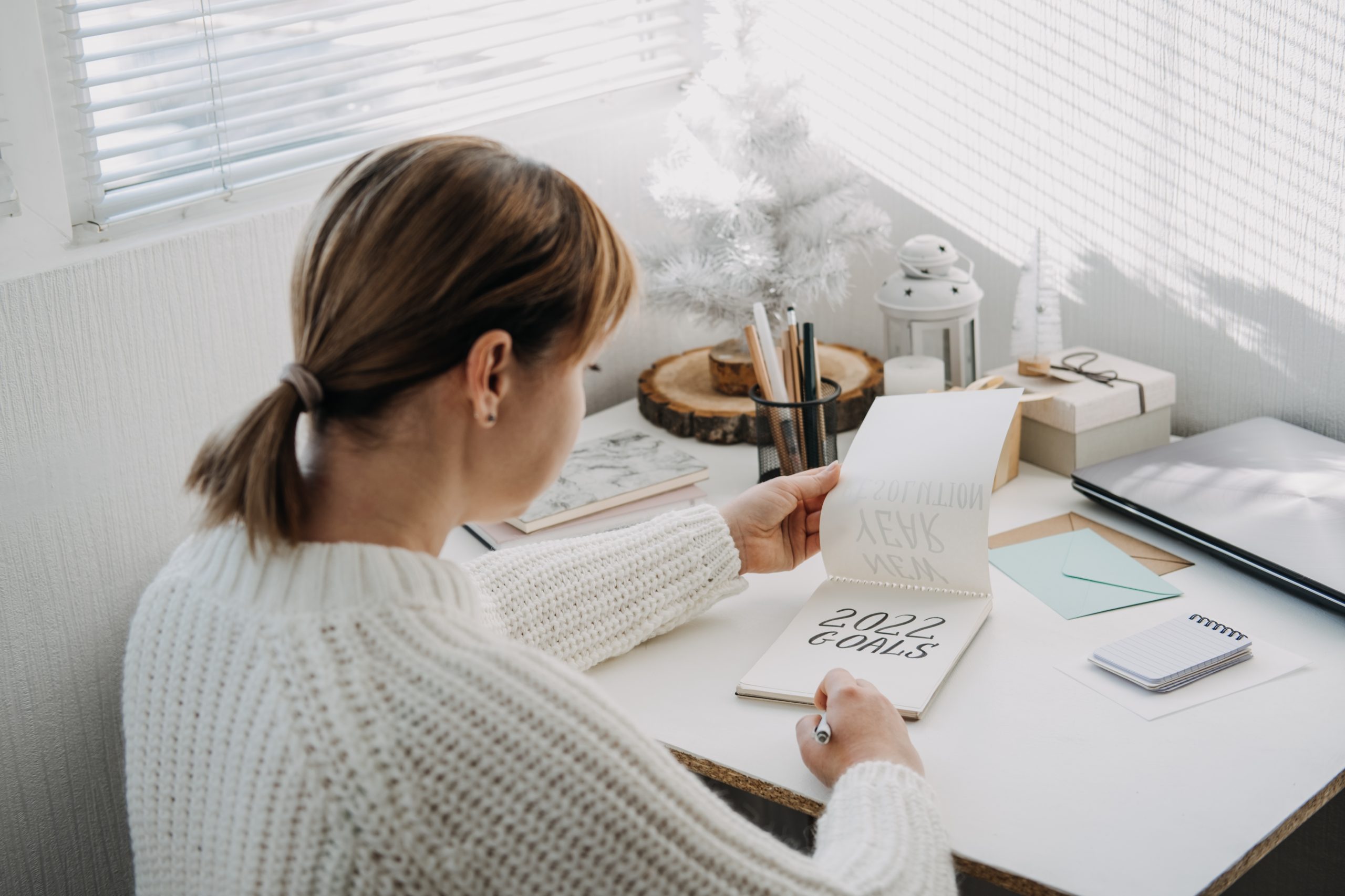 2022 goals, New year resolution. Woman in white sweater writing Text 2022 goals in open notepad on the table. Start new year, planning and setting goals for the next year.